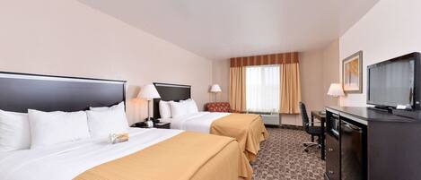 A hotel room with two beds, a desk, a television, and a window with curtains.