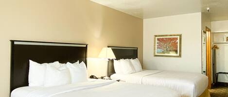 A hotel room with two beds, a nightstand with a lamp, a painting on the wall, and a mirror.