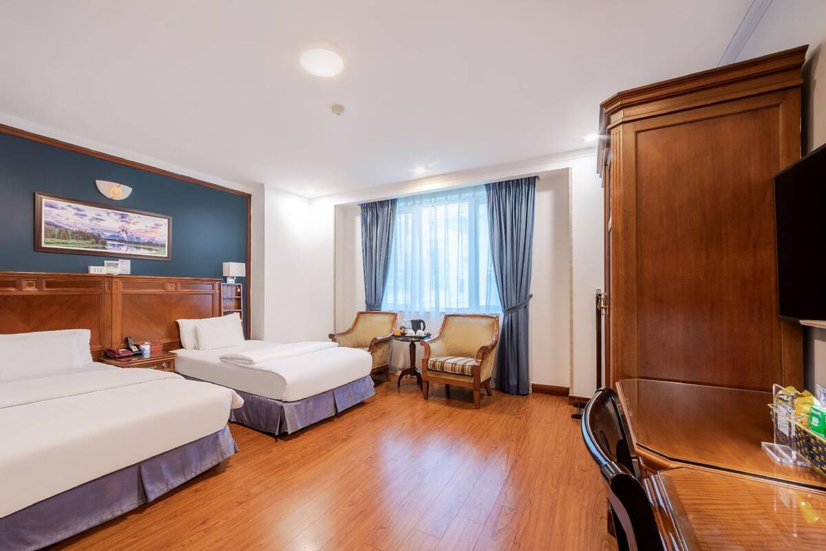 A hotel room with two beds, a desk, a chair, a television, and a large wooden wardrobe.