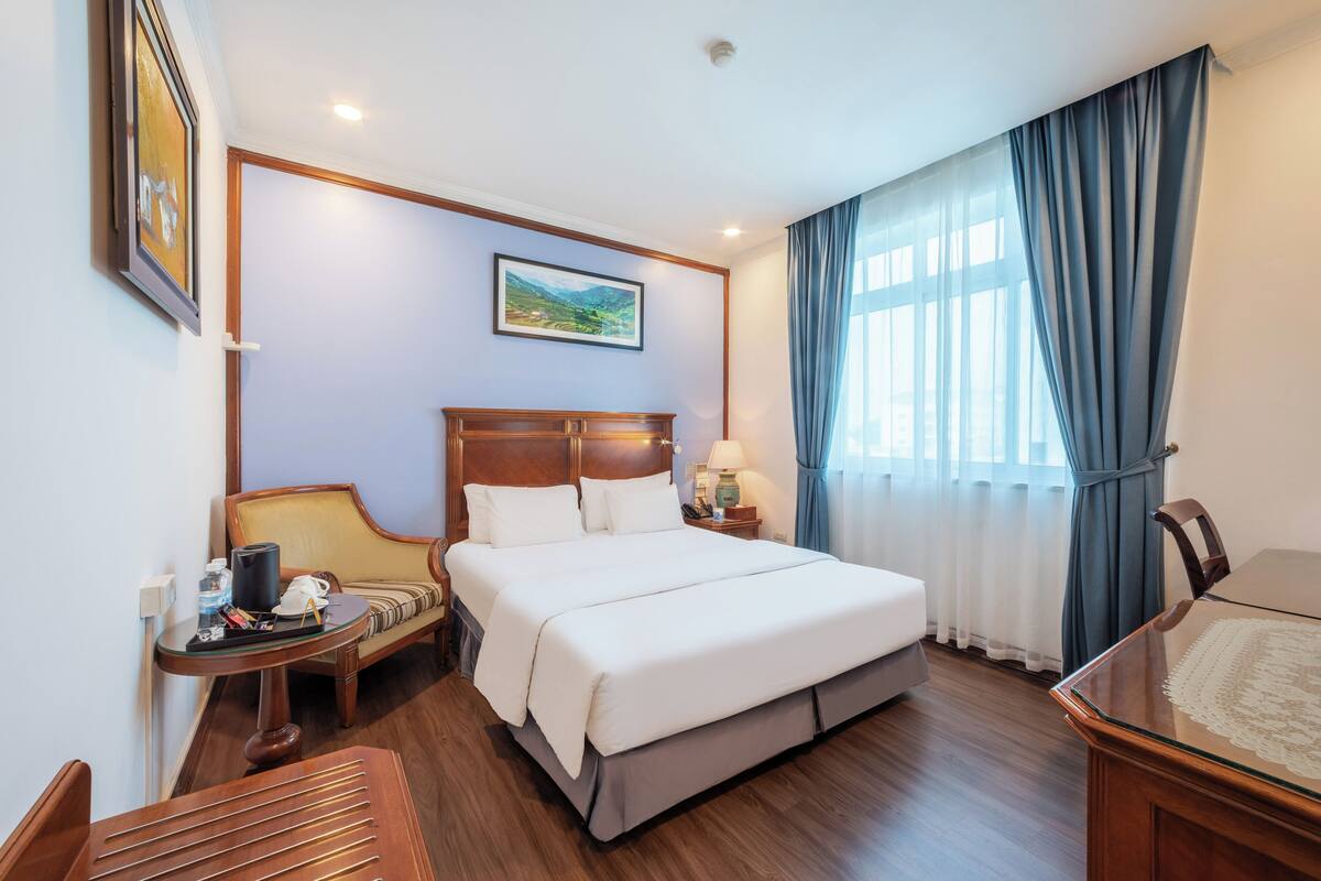 A hotel room with a large bed, a wooden headboard, a desk, and a chair.
