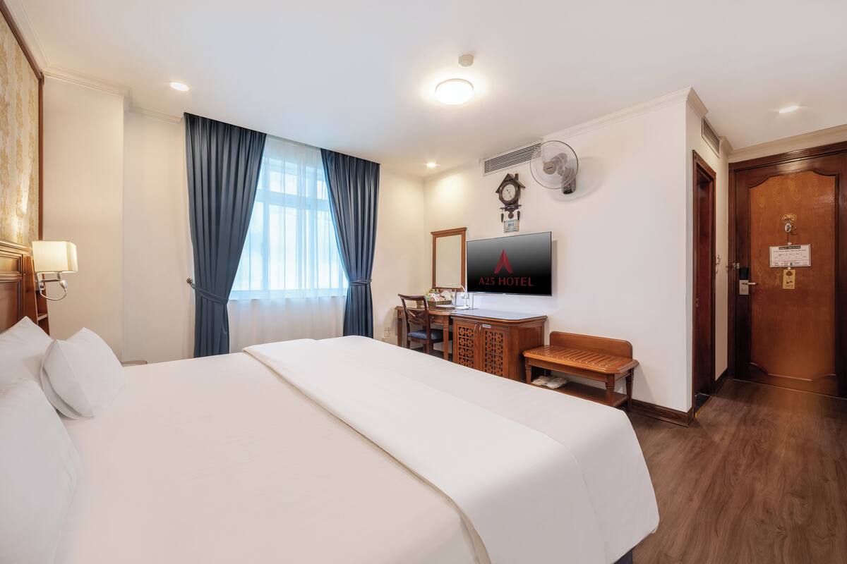 A hotel room with a large bed, a desk with a chair, a television, and a wooden door.