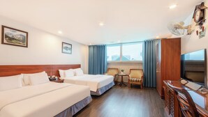 Habitación de hotel con dos camas, un escritorio con televisor, una silla, una mesita con una planta y una ventana con cortinas.