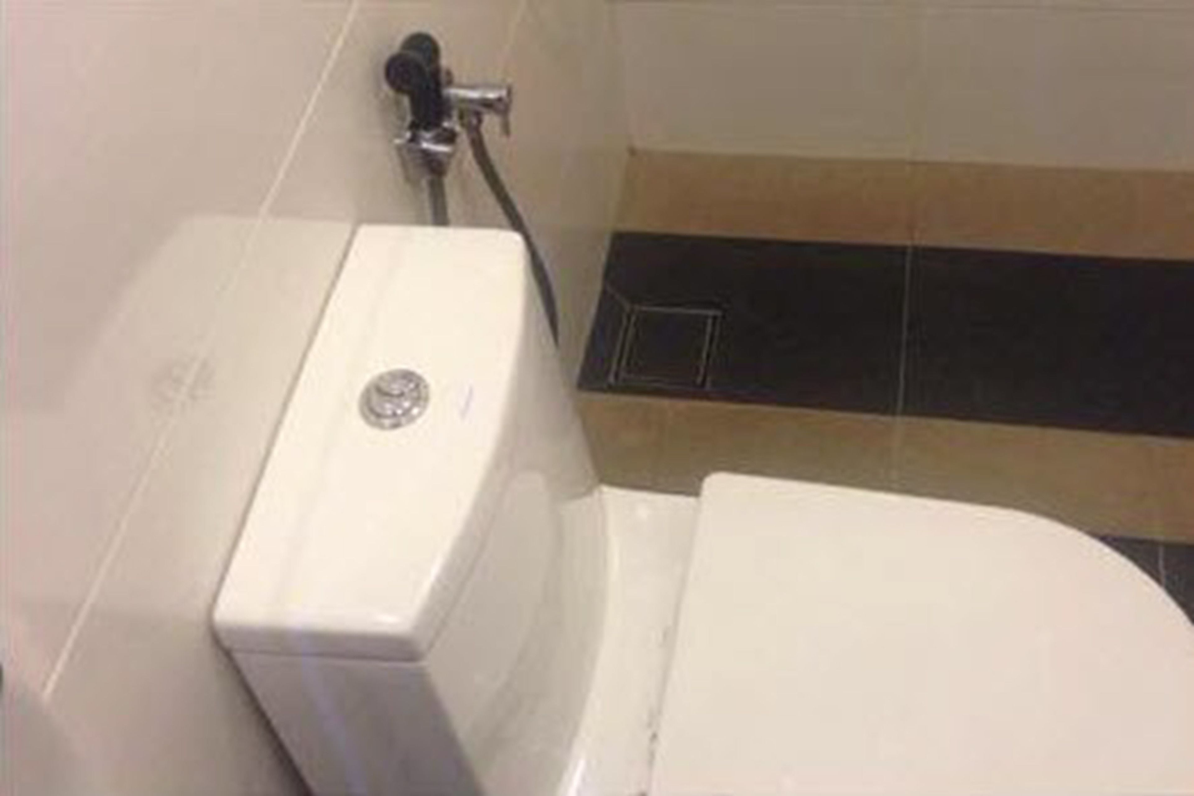 A bathroom with a white toilet, a shower area, and a tiled floor with a black and beige pattern.