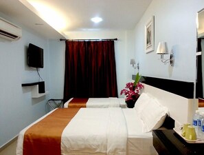 Habitación de hotel con dos camas, un televisor, una lámpara de pared y un florero.