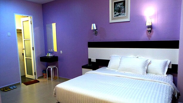 A bedroom with a bed, a nightstand, a bedside table, a mirror, and a door leading to another room. - Hotel Star Moon (Malacca City)