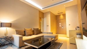 Un salon moderne avec un canapé, une table basse et une lampe. On y trouve une porte qui mène à une autre pièce, ainsi qu’une petite table sur laquelle sont posées des bouteilles.