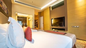 Une chambre d’hôtel dotée d’un grand lit, d’un téléviseur à écran plat, d’un dressing et d’une salle de bain visible à travers une porte ouverte.