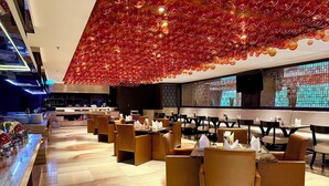 Un restaurant moderne doté d’un plafond haut orné de sphères de verre rouge, d’un plancher en bois et d’un bar avec des tabourets.
