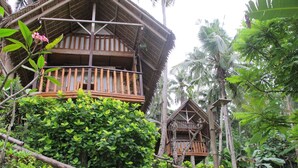 A traditional wooden house with a balcony, surrounded by lush greenery and palm trees. - Coco Beach Island Resort (Puerto Galera)