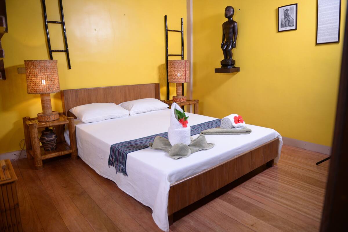 A neatly made bed with white linens, two bedside lamps, and a wooden headboard.