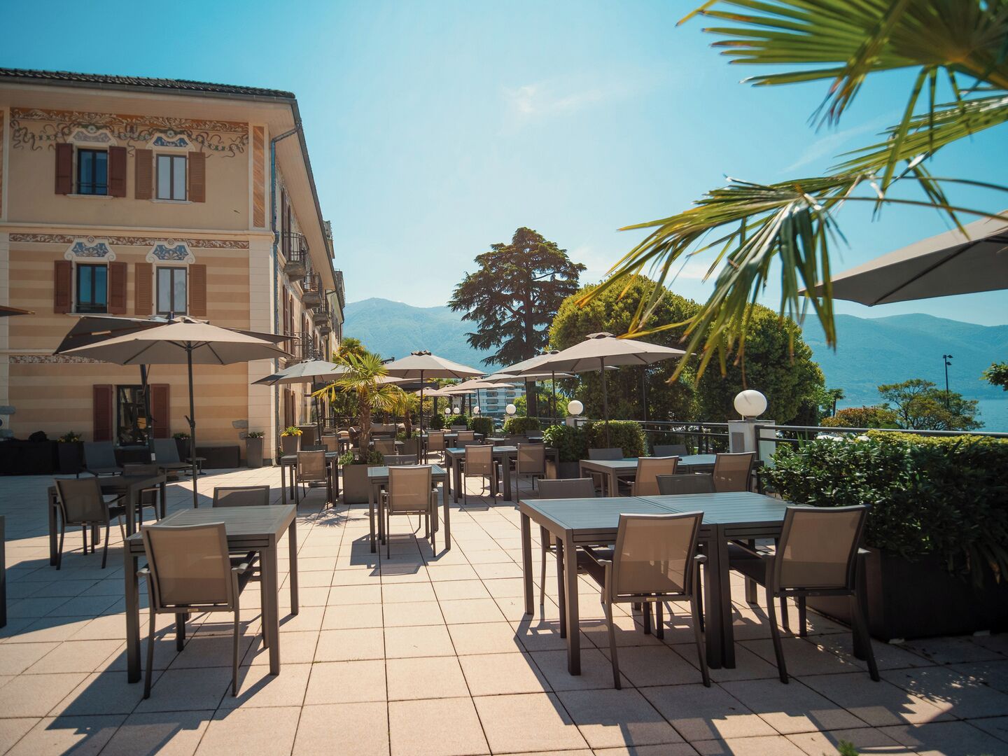 An outdoor patio with tables and chairs, umbrellas, and a view of mountains.