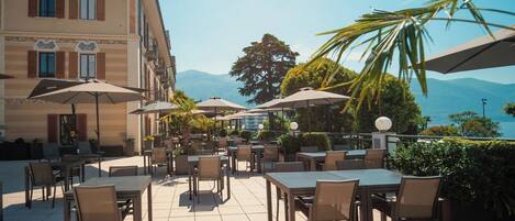 An outdoor patio with tables and chairs, umbrellas, and a view of mountains.