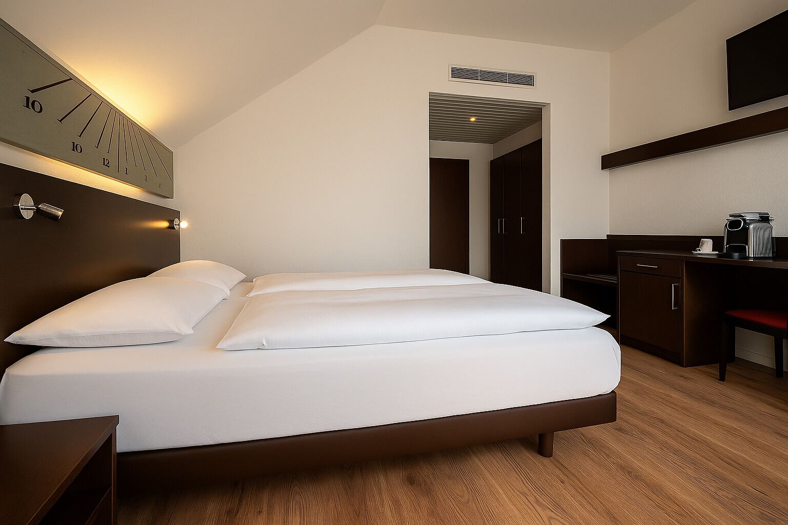 Una habitación de hotel moderna con cama, mesitas de noche, un escritorio y un reloj en la pared.