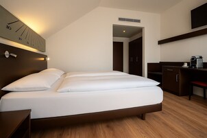 Una habitación de hotel moderna con cama, mesitas de noche, un escritorio y un reloj en la pared.