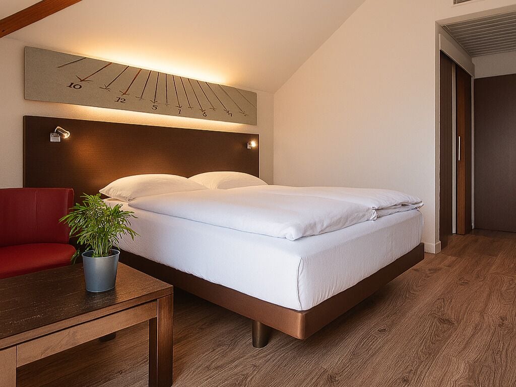 Une chambre d’hôtel moderne avec un lit, une chaise rouge, une petite table et une plante en pot.