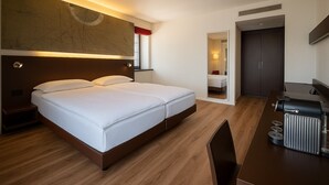 A modern hotel room with a large bed, a desk with a grill, and a wardrobe.