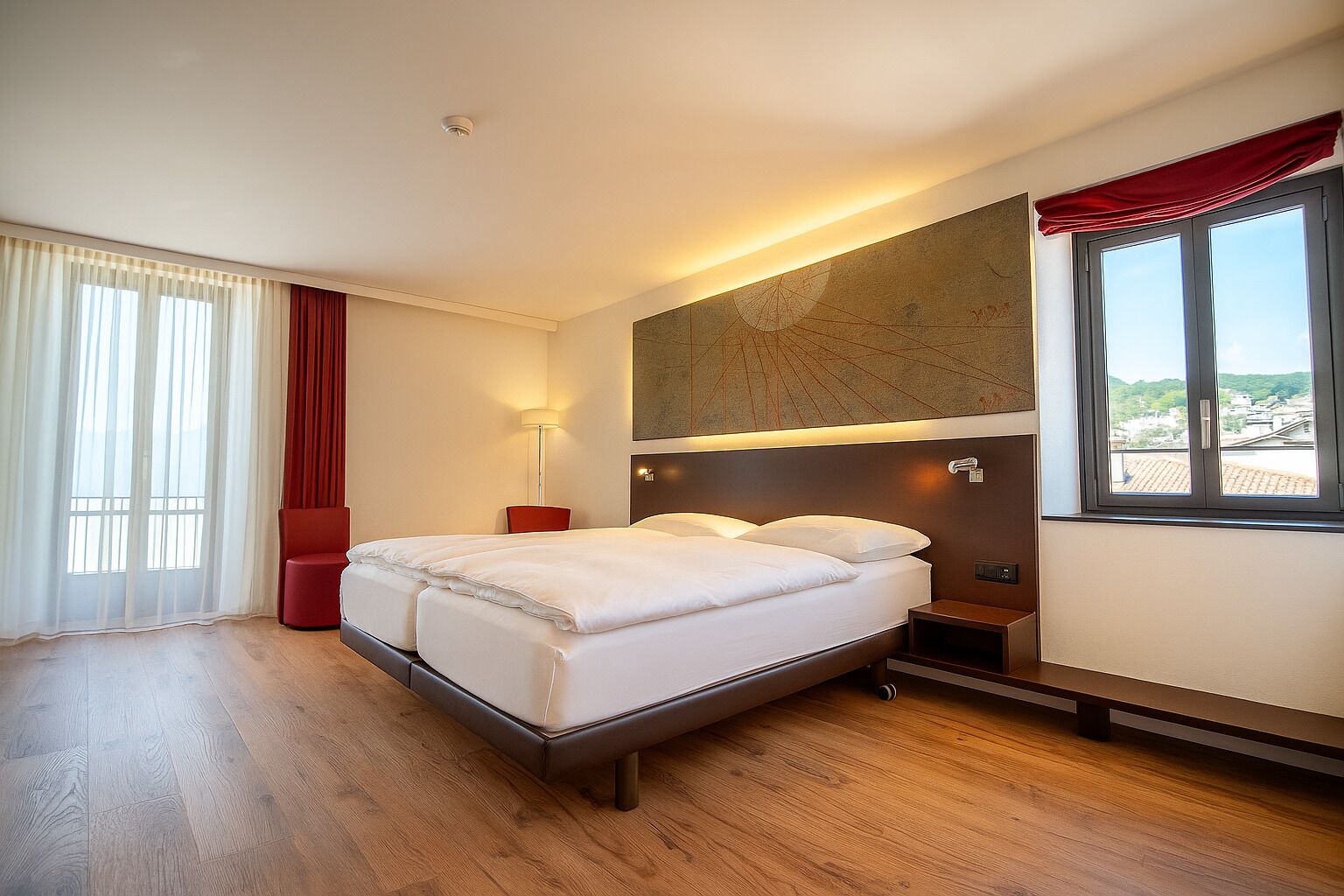Habitación de hotel con una cama doble, una mesita de noche, una lámpara, una ventana con vistas y una cortina roja.