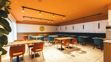 Un restaurante con varias mesas y sillas, un techo con luces colgantes y una pared con un logotipo circular.