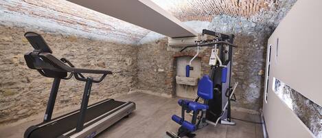 A home gym with a treadmill and weight equipment, located in a room with exposed brick walls and a sloped ceiling.