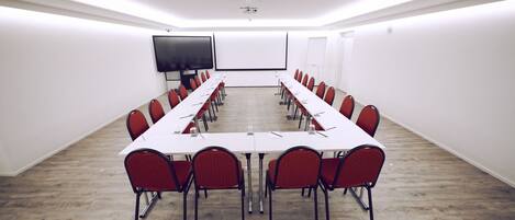 A conference room with a long table, red chairs, a projector screen, and a whiteboard.