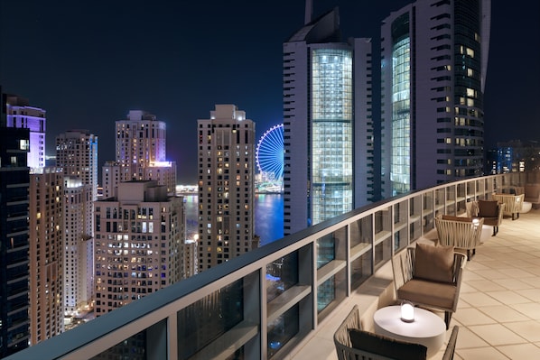 Terraza en la azotea con mobiliario exterior y vista al horizonte urbano nocturno.