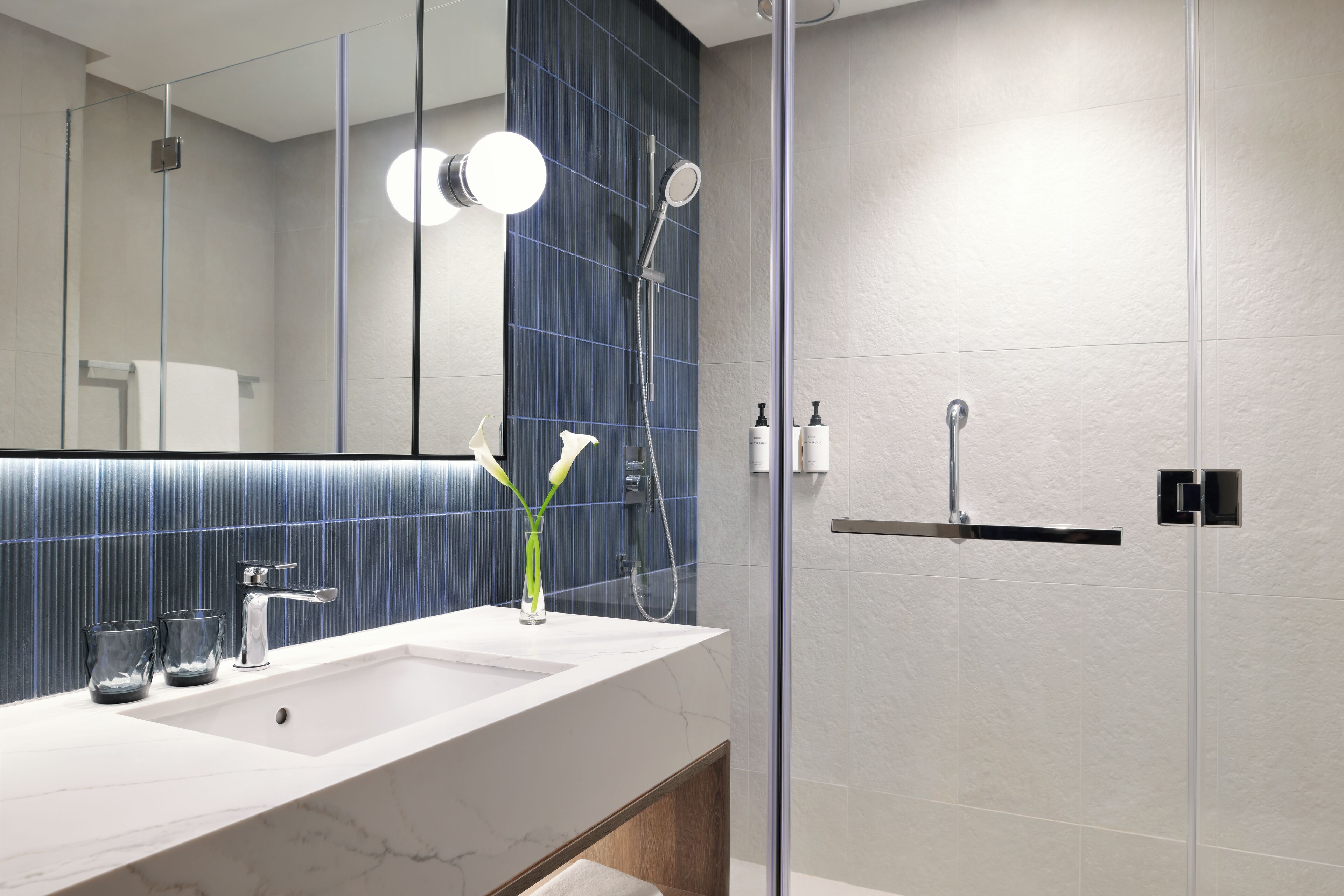 Une salle de bain moderne avec un grand miroir, deux lavabos et un espace douche.