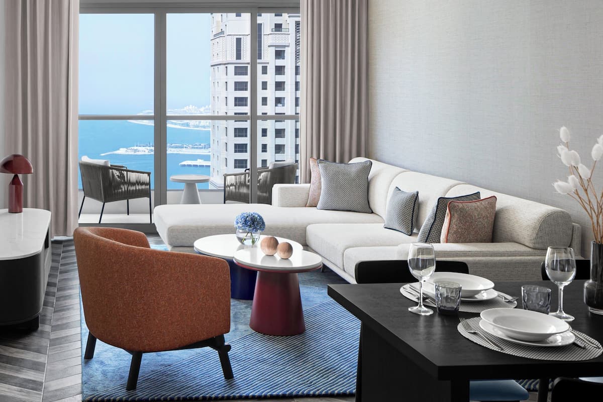 A modern living room with a sofa, armchairs, a dining table set for two, and a view of the cityscape.