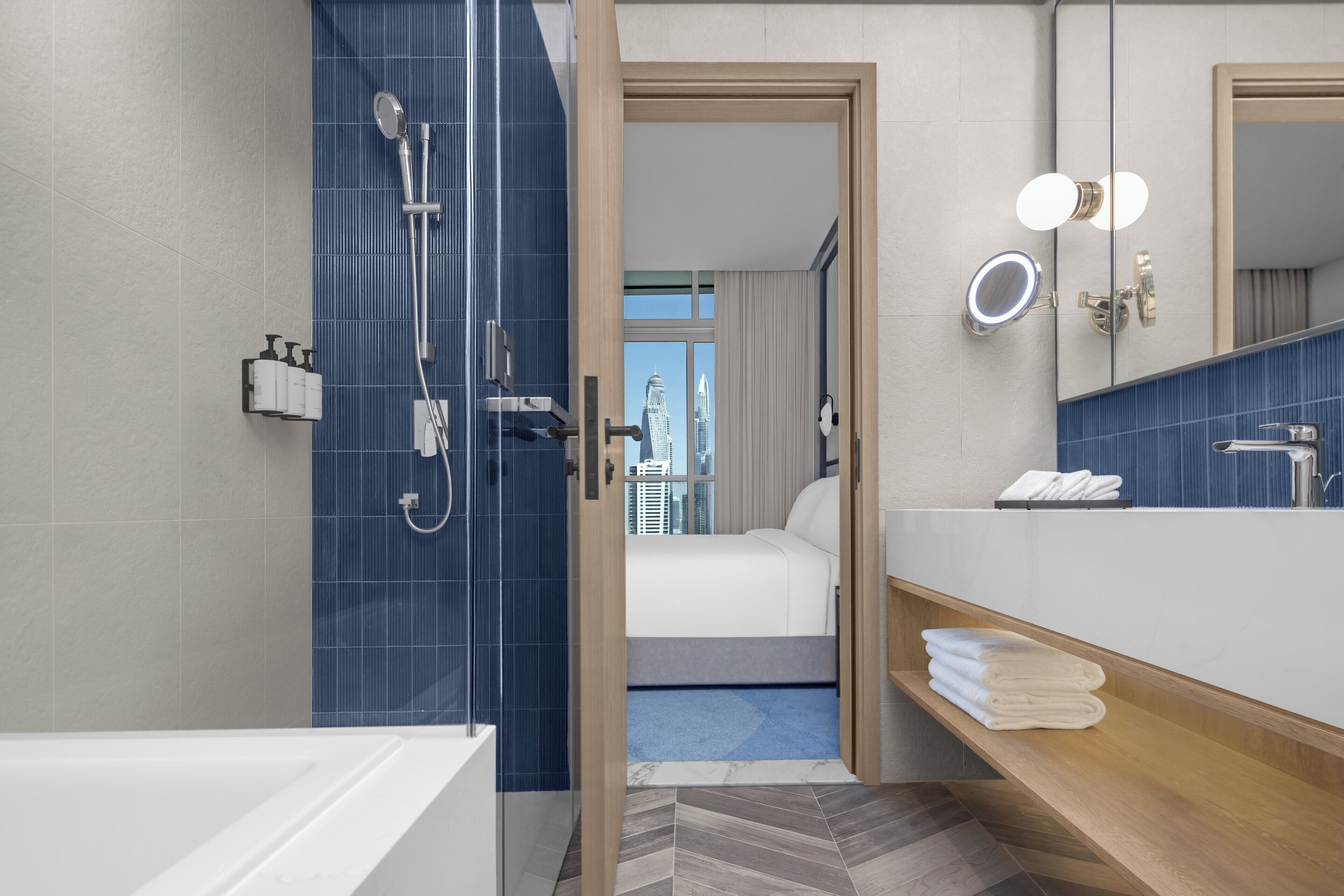 A modern bathroom with a shower, a bathtub, a vanity with a mirror, and a view of a cityscape through an open door.