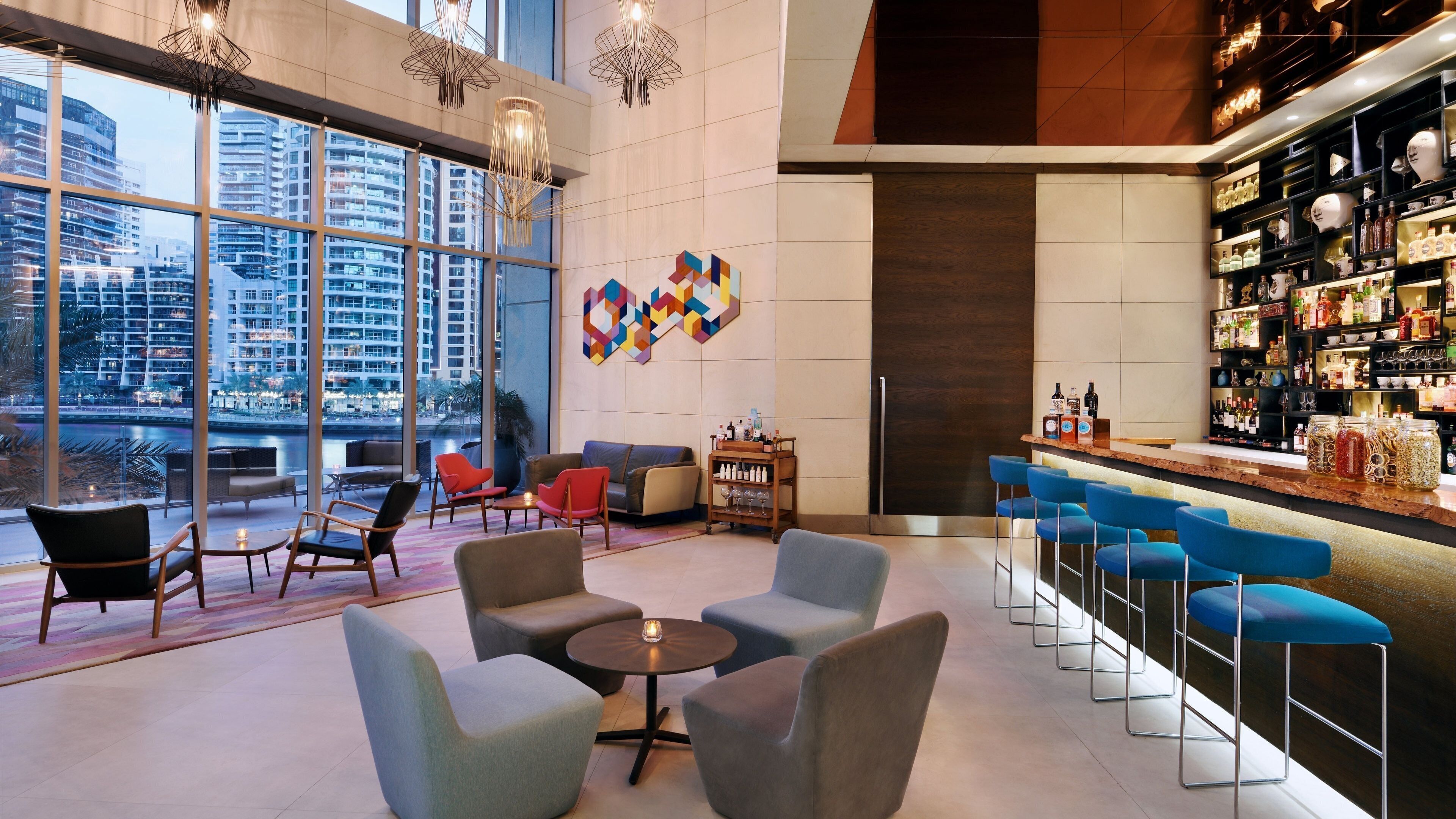 A modern bar area with seating, a bar counter, and a view of the cityscape through large windows.
