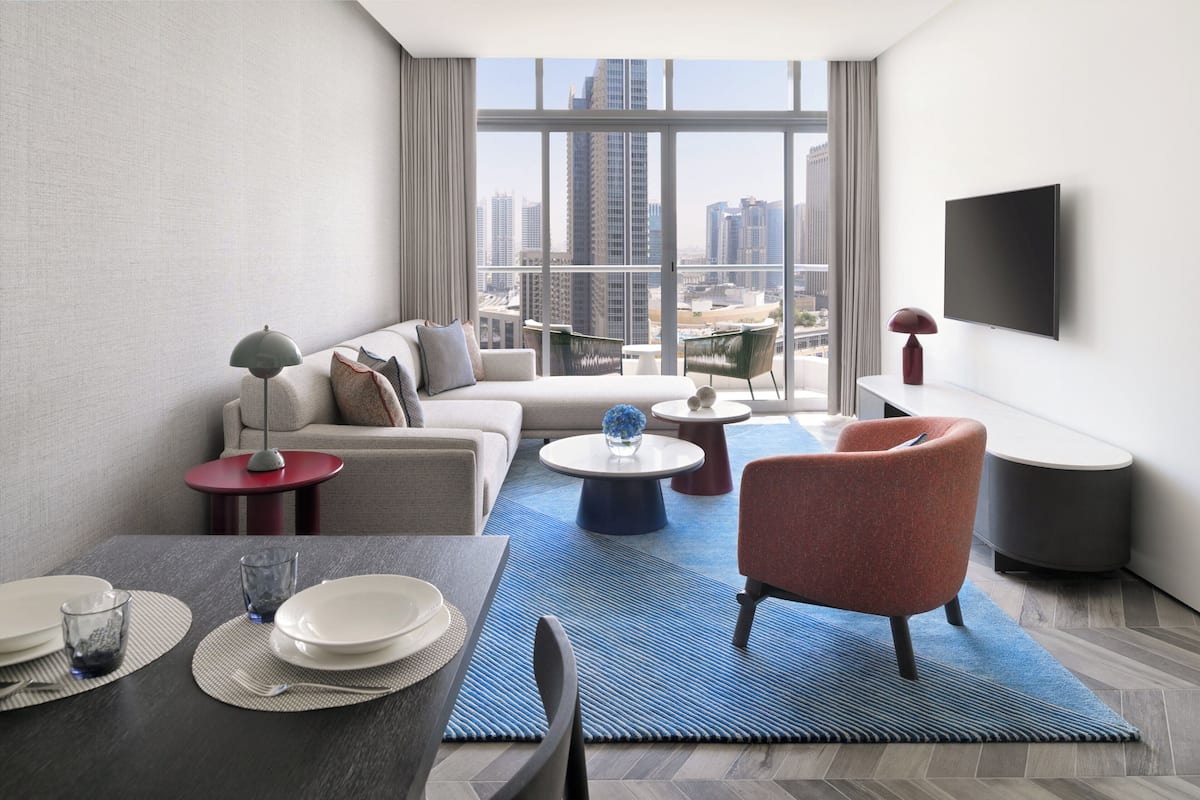 A modern living room with a sofa, armchairs, a dining table with plates and glasses, and a large window with a city view.
