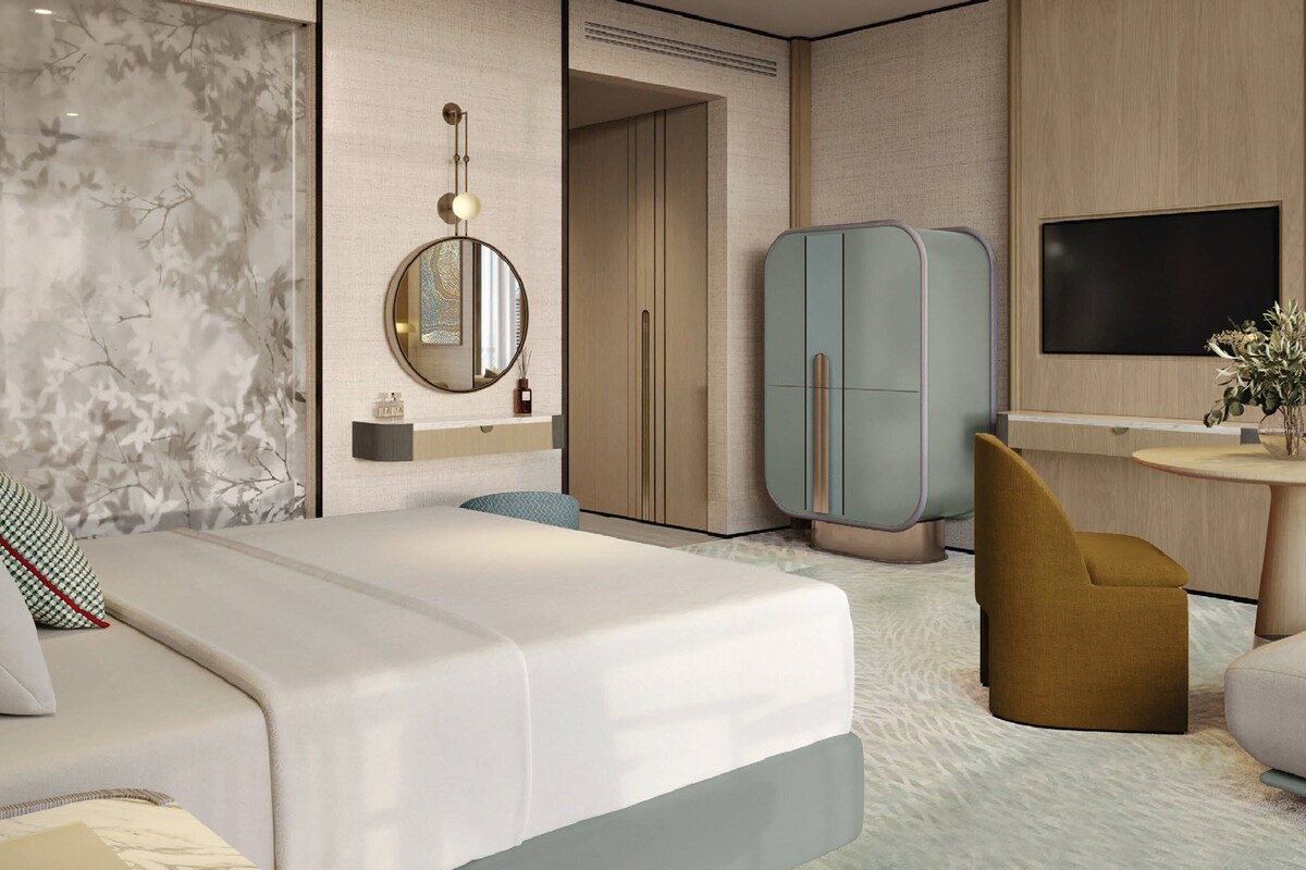 A modern hotel room with a bed, a round table, a sofa, a wardrobe, a mirror, and a TV.
