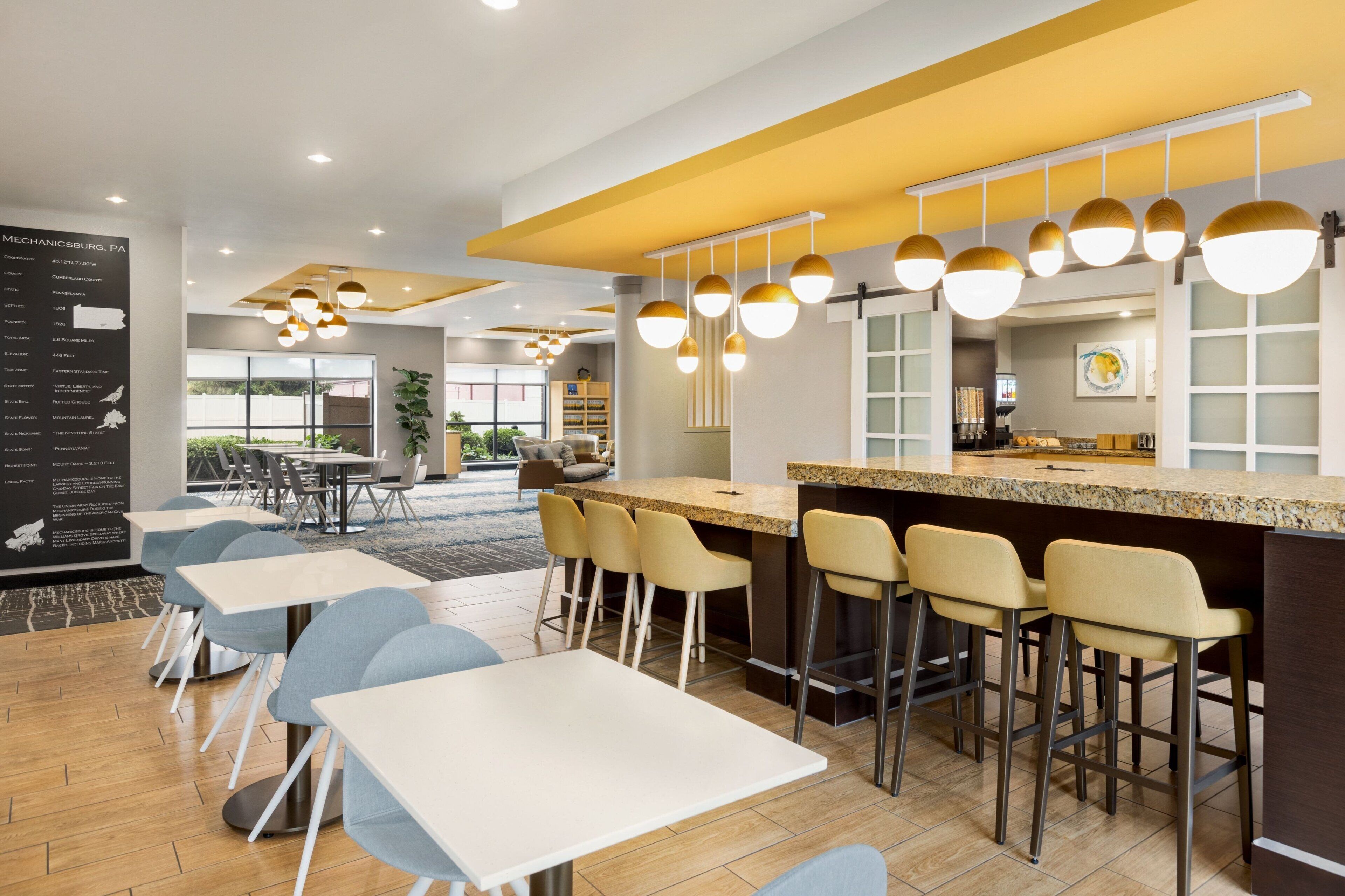 A modern hotel lobby with a bar area, seating arrangements, and a large informational poster.