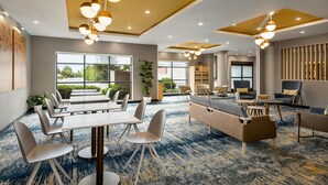 Un hall d’hôtel moderne, doté d’un tapis bleu, de coins salon et de grandes fenêtres donnant sur un paysage verdoyant.