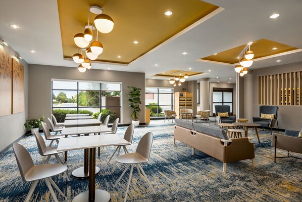 Un hall d’hôtel moderne, doté d’un tapis bleu, de coins salon et de grandes fenêtres donnant sur un paysage verdoyant.