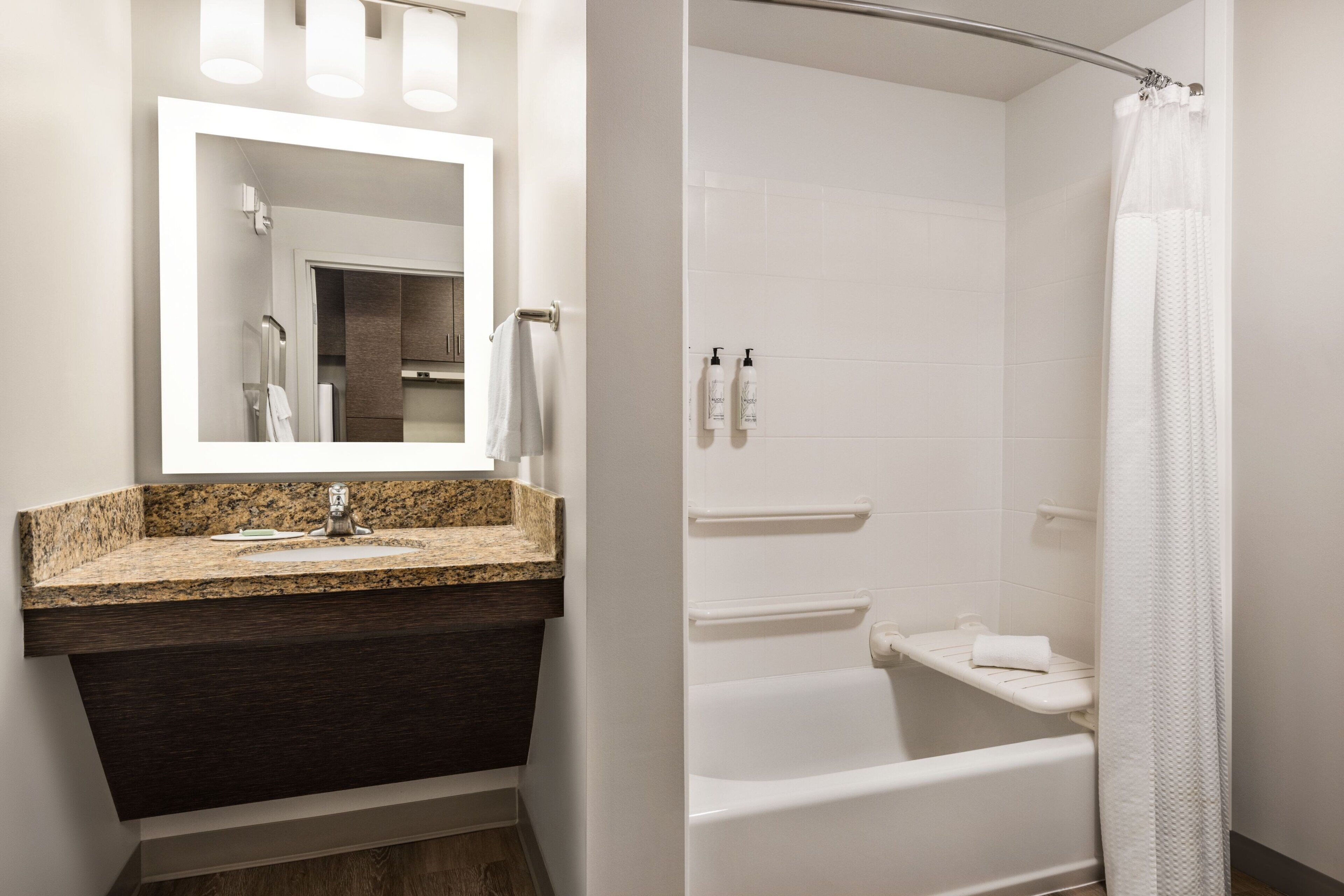 Bany amb un lavabo de superfície de granit, un mirall, dutxa amb cortina i una banyera blanca.