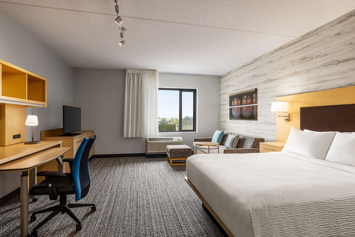 Habitación de hotel con cama, escritorio, silla y ventana con cortinas.