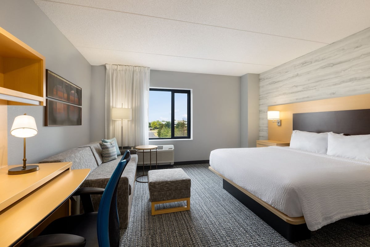 Habitación de hotel moderna con una cama grande, un escritorio con lámpara, un sofá y vistas al exterior.