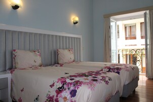 Una cama doble con ropa de cama floral, un cabecero y dos lámparas fijadas a la pared.