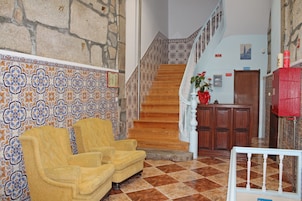 Un hall de hotel con piso a cuadros, una escalera, un mueble de madera y un sillón amarillo.