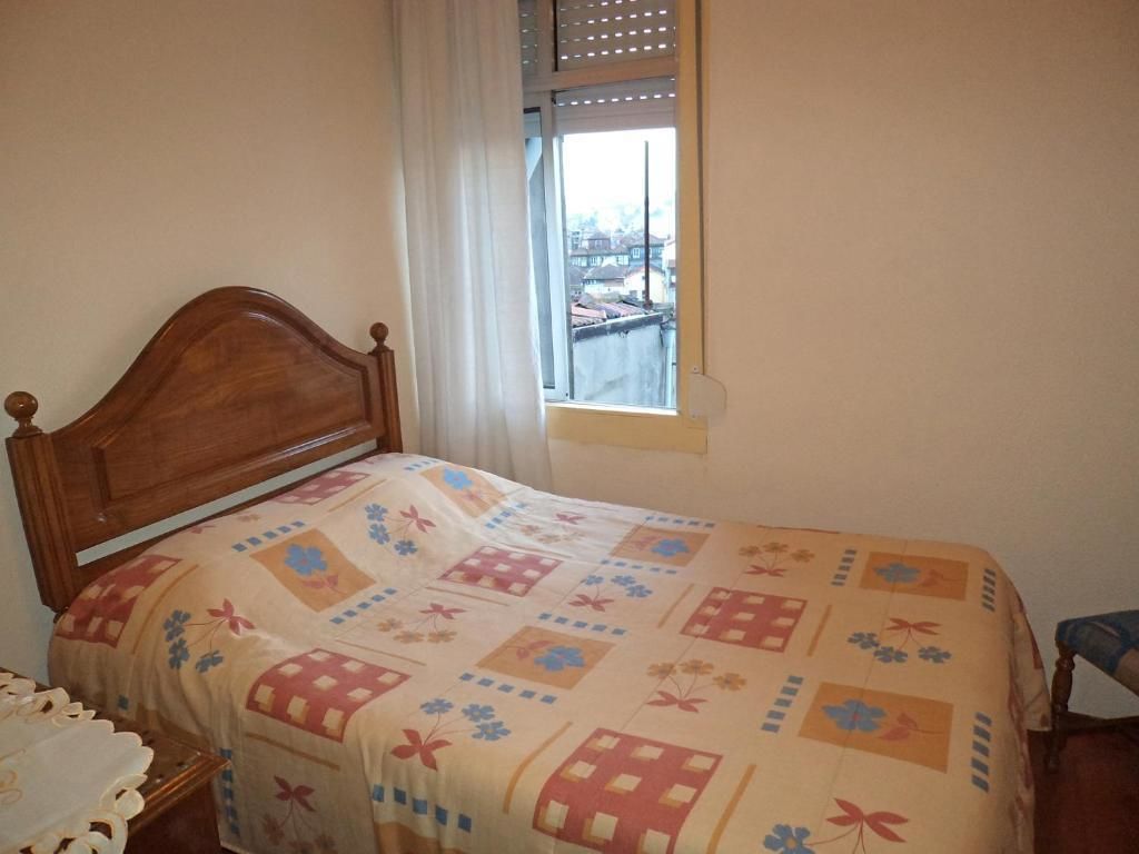 A bedroom with a wooden bed, a window with a view, and a small table.