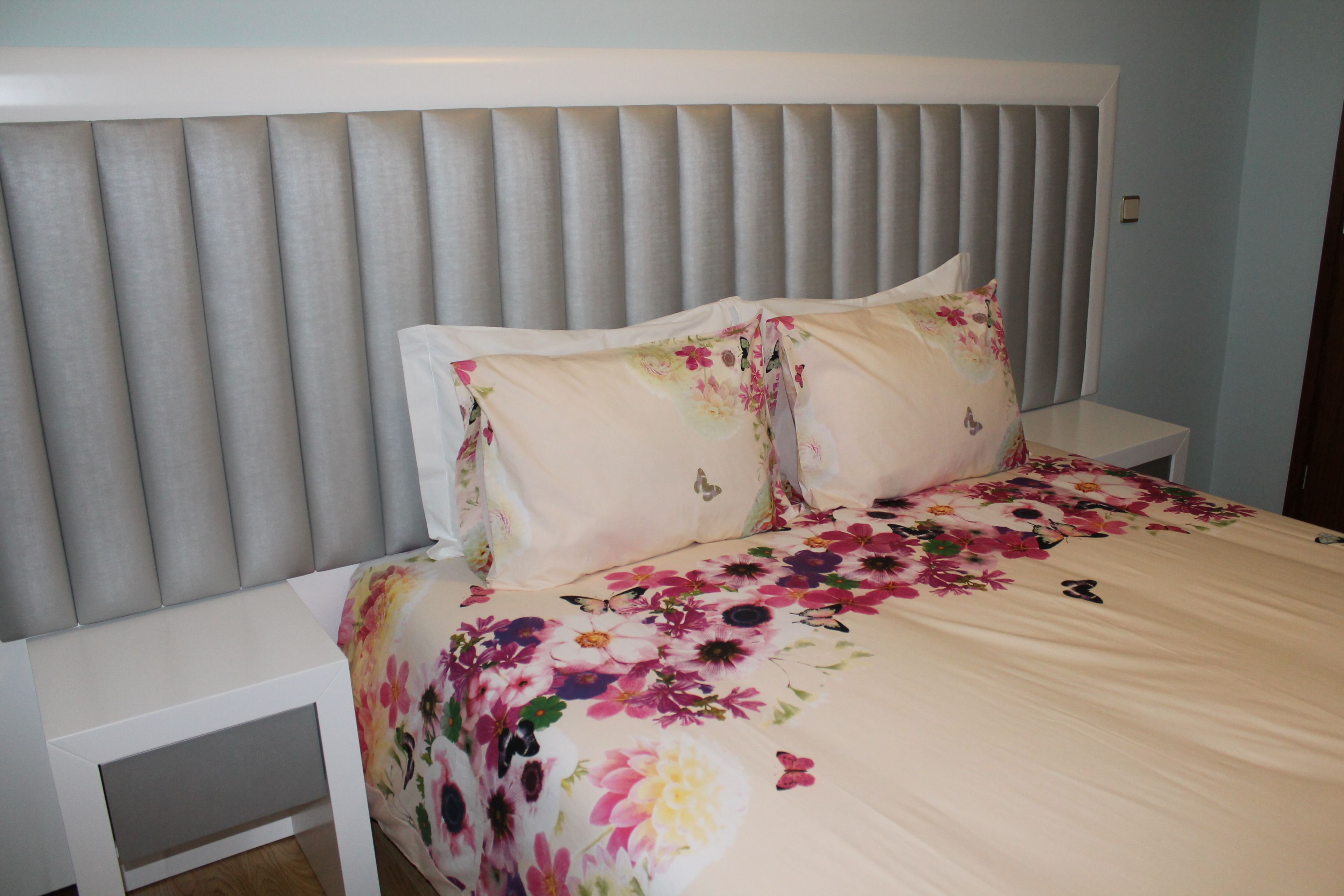 A bed with a floral bedspread and two pillows, a headboard, and a nightstand.