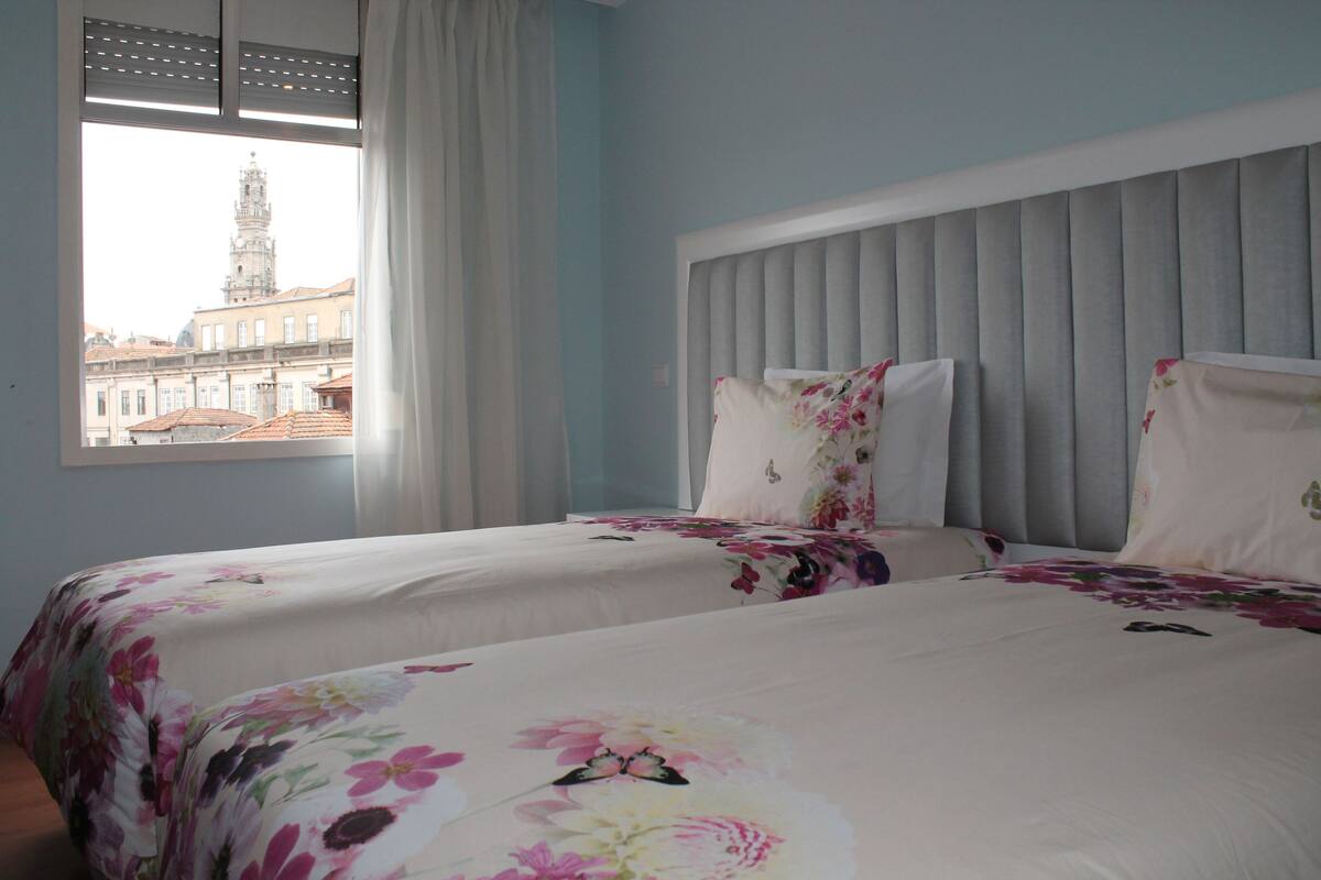 Een hotelkamer met twee bedden, een groot raam en uitzicht op een stadsbeeld.