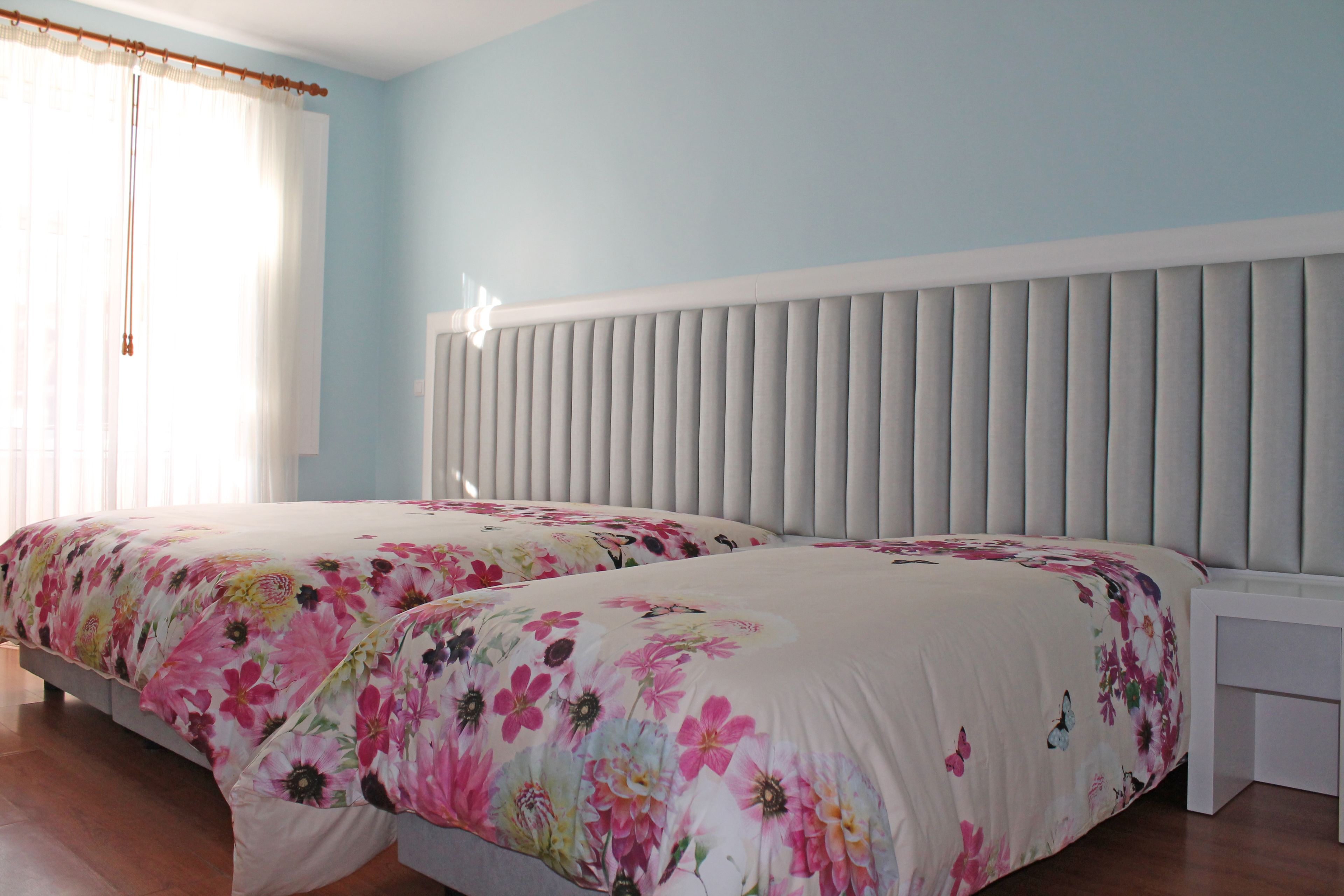 A bedroom with two beds, a white headboard, and a window with curtains.