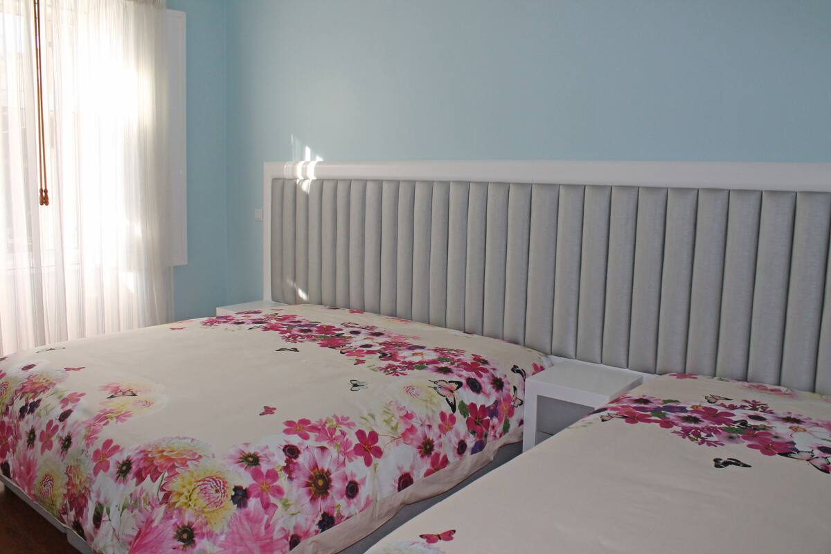 Een slaapkamer met twee bedden, een wit hoofdeinde en een bloemenbedekking.