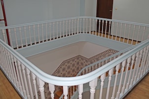 Una habitación con barandilla blanca, alfombra estampada y suelo de madera.