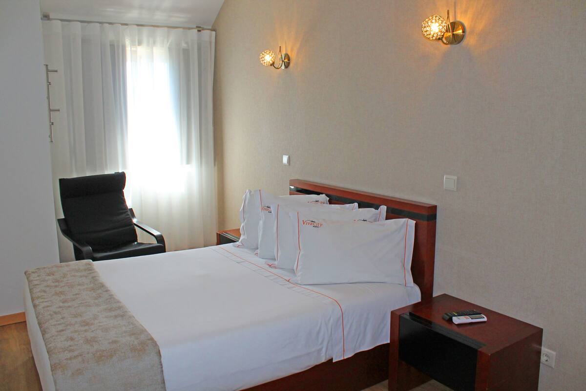 Une chambre d’hôtel comprenant un lit, une chaise, une table de chevet et deux lampes fixées au mur.