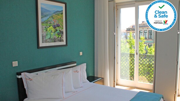 Una habitación de hotel con cama, mesita de noche, un cuadro enmarcado en la pared y vista al exterior a través de una puerta corrediza de vidrio.