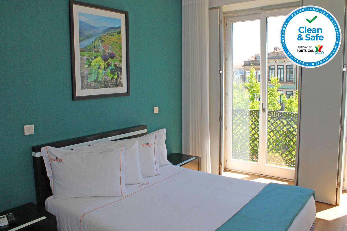 Une chambre d’hôtel avec un lit, une table de chevet, un tableau encadré au mur et une vue sur l’extérieur par une porte-fenêtre coulissante.