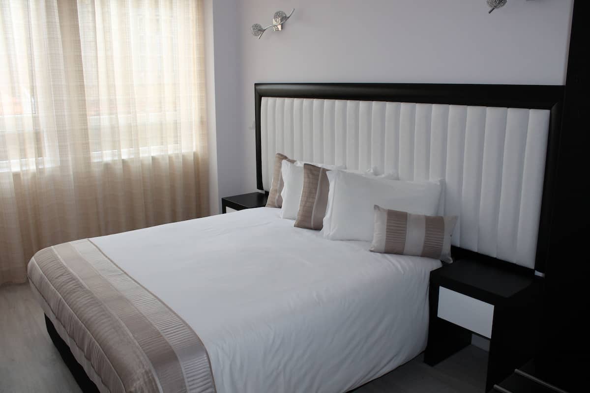 Un lit bien fait, recouvert d’une couvre-lit à rayures blanches et beiges, avec une tête de lit noire et deux tables de chevet dotées de tiroirs.