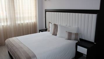 Una cama bien hecha con un edredón blanco y beige a rayas, un cabecero negro y dos mesitas de noche con cajones.